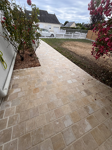 Allée de pavés en pierre naturelle devant une maison avec roses.