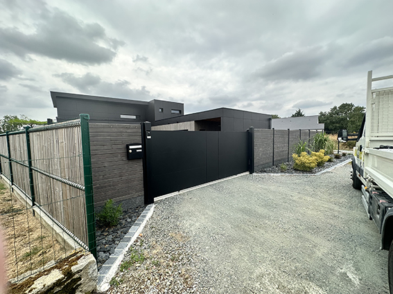 Portail d'entrée moderne en aluminium noir devant une maison contemporaine avec clôture en bois