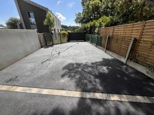 Enrobé avec une ligne de pavés devant une maison moderne avec clôture en bois