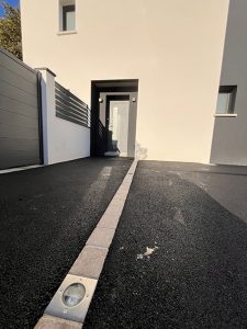 Entrée moderne d'une maison avec allée asphaltée et éclairage intégré.
