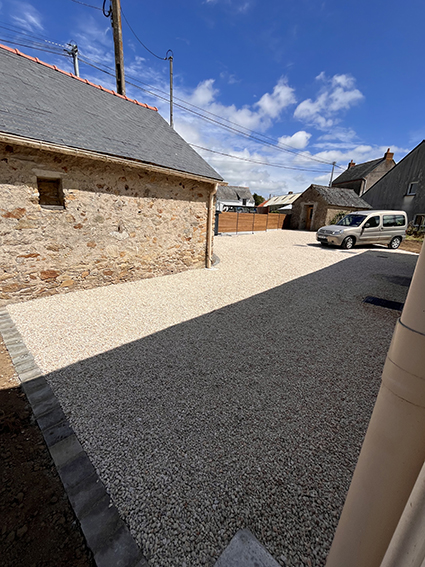 Gravel driveway leading to a stone building and a parked car
