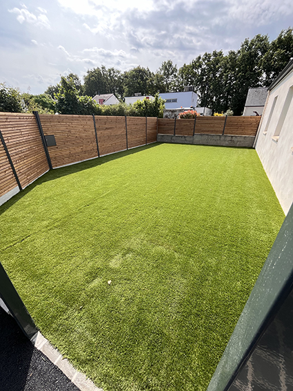 Pelouse artificielle verte avec clôture en bois dans un jardin.